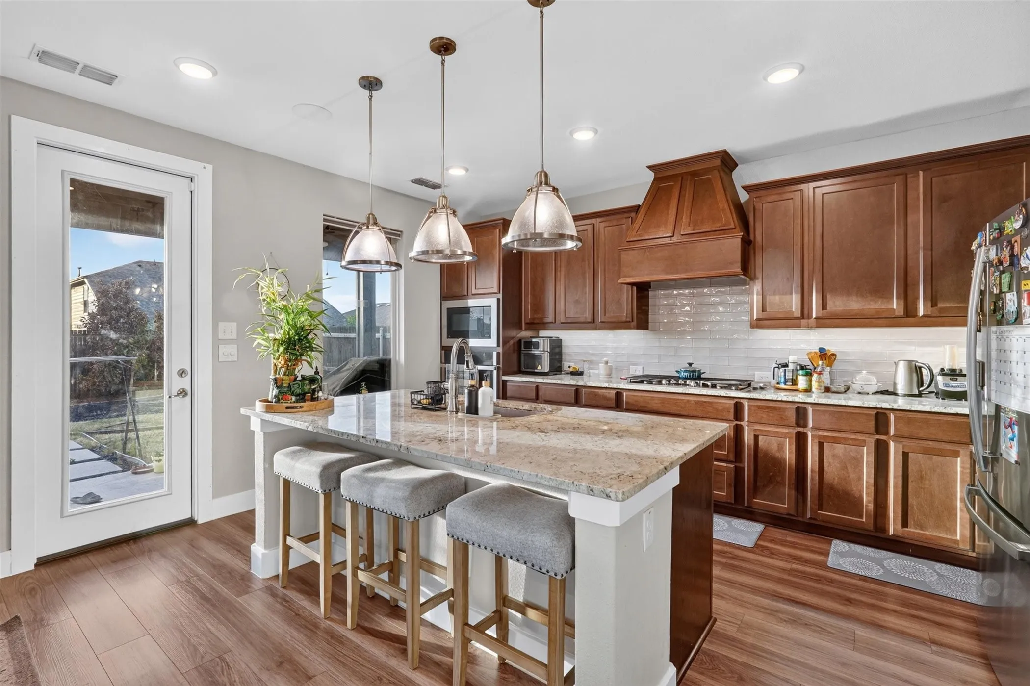 Kitchen featuring wood-finish flooring, an oversized island with seating, pendant lighting, wood cabinetry, and a full-light door with exterior access