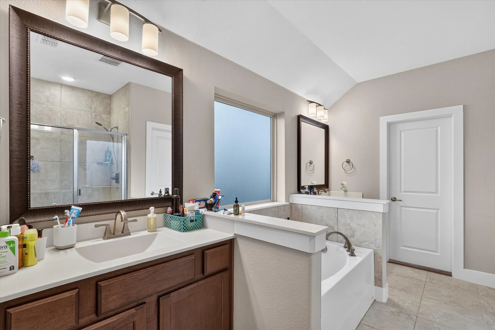 Bathroom featuring a double vanity, large soaking tub, glass-enclosed shower, and vaulted ceiling
