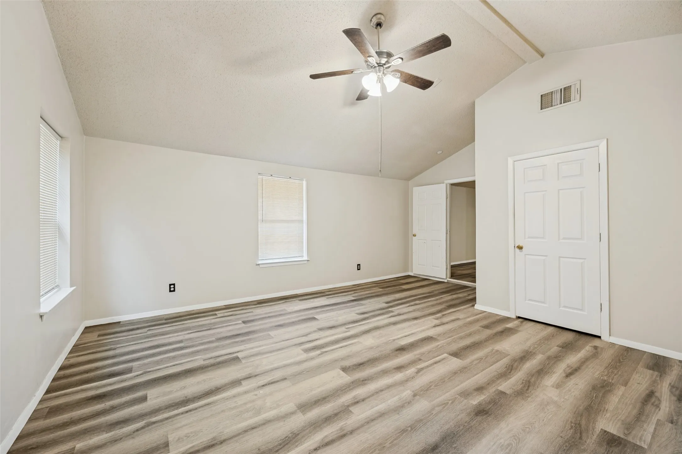 Spacious room featuring vaulted ceilings, wood-finish flooring, two windows, and a ceiling fan