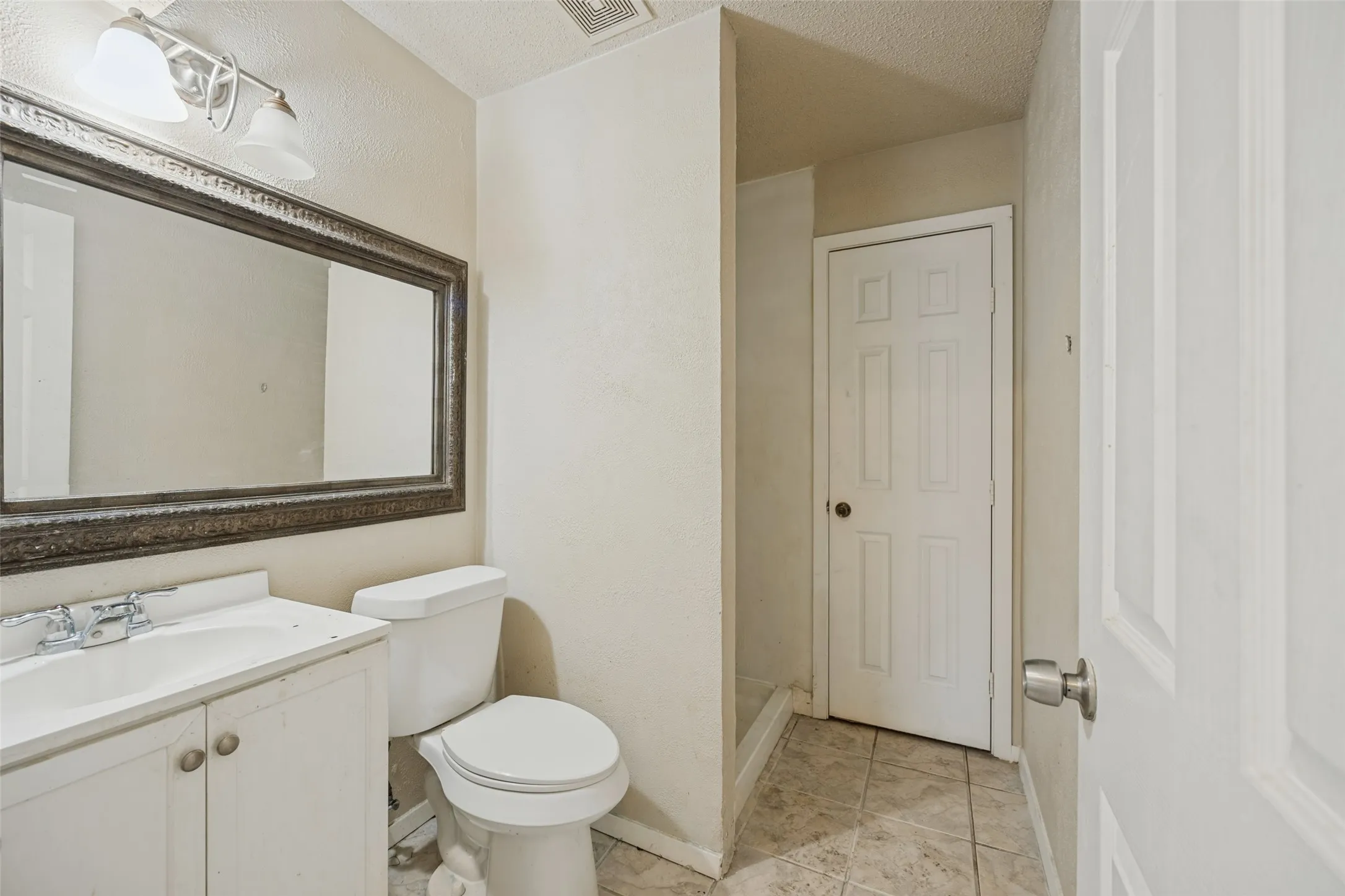 Vanity with integrated sink, framed mirror, two-light fixture, toilet, and tiled flooring