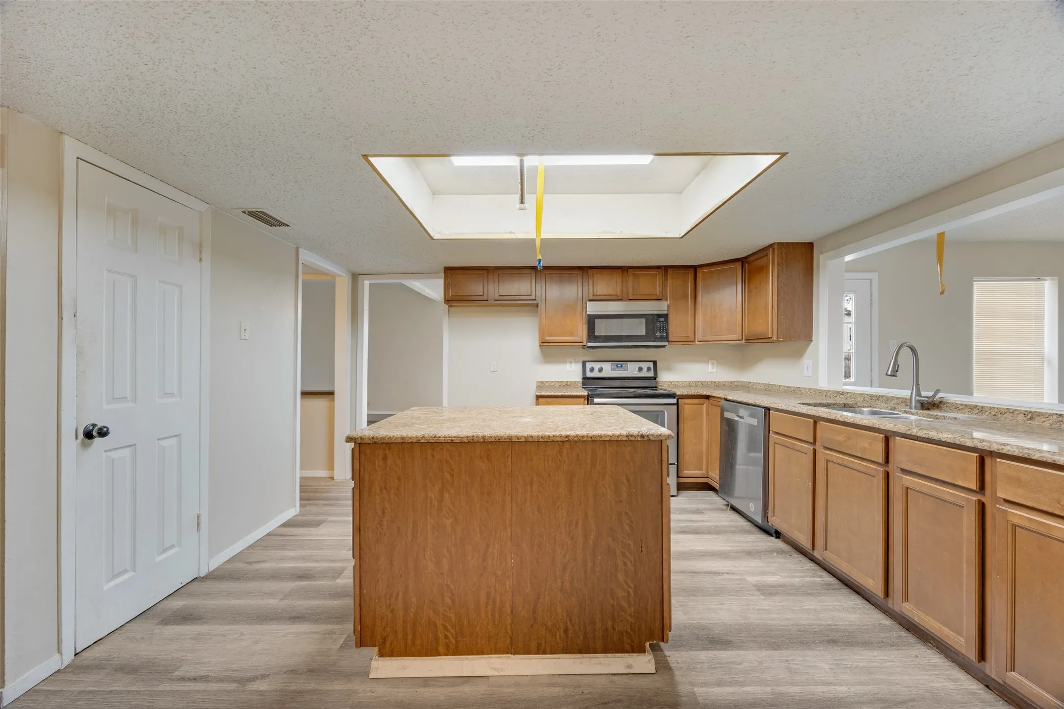 Kitchen featuring wood-finish flooring, wood cabinetry, stainless steel appliances, a center island with a stone countertop, and a skylight
