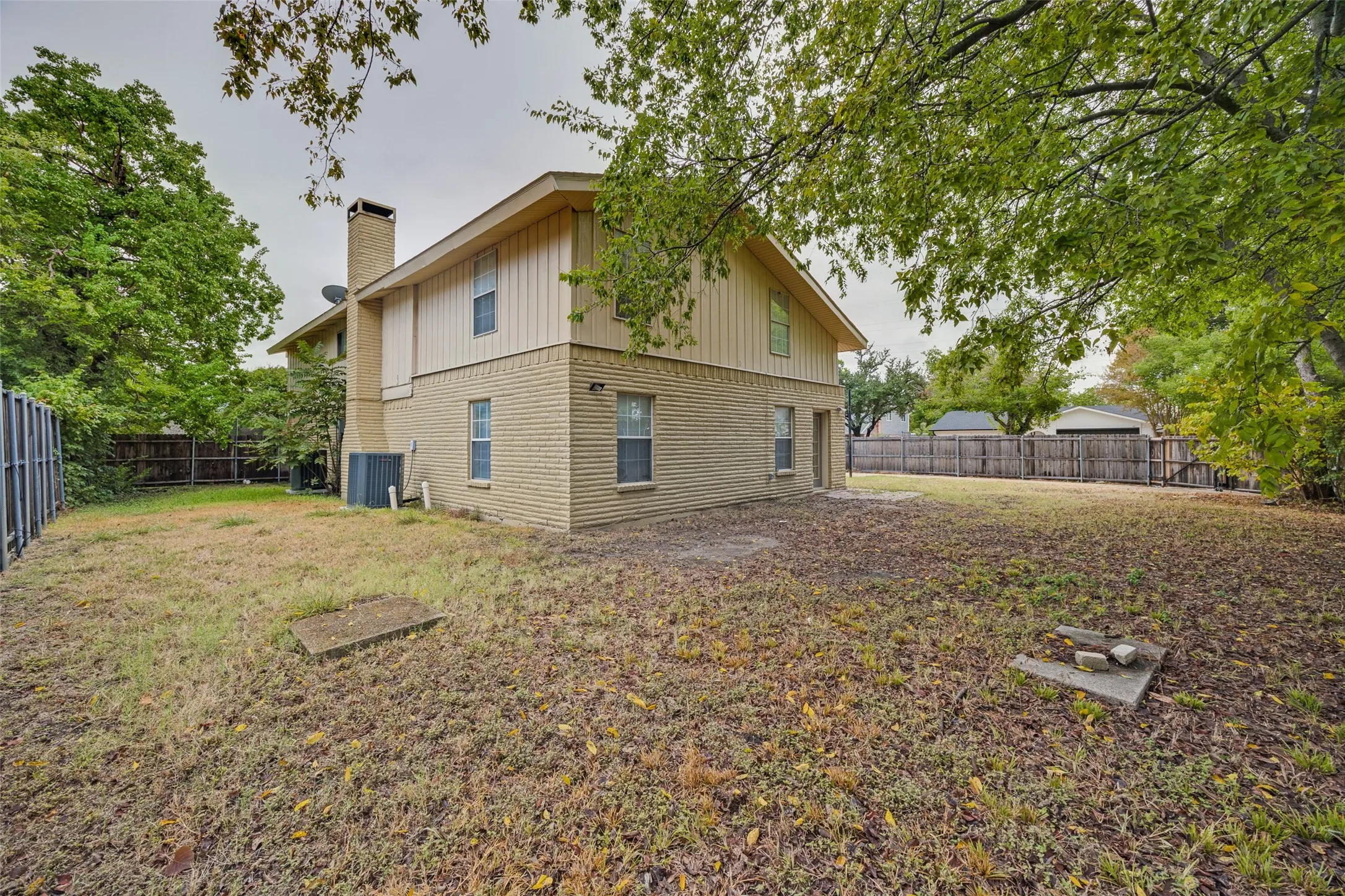 Expansive rear yard featuring a brick and wood-sided exterior, a brick chimney, and a privacy fence