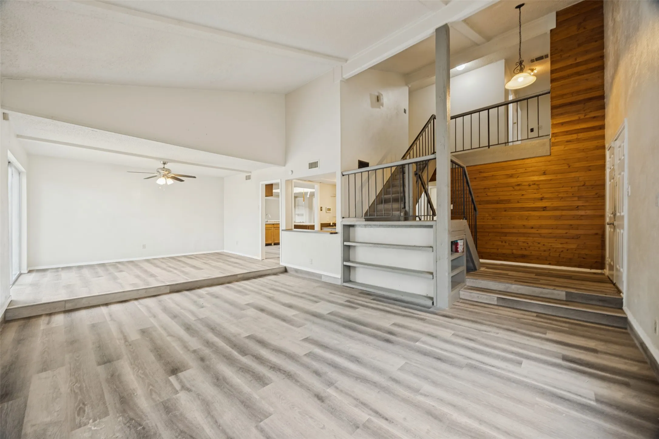 Vaulted ceilings, wood-finish flooring, staircase with metal railing, built-in shelving, and a wood-paneled wall accent