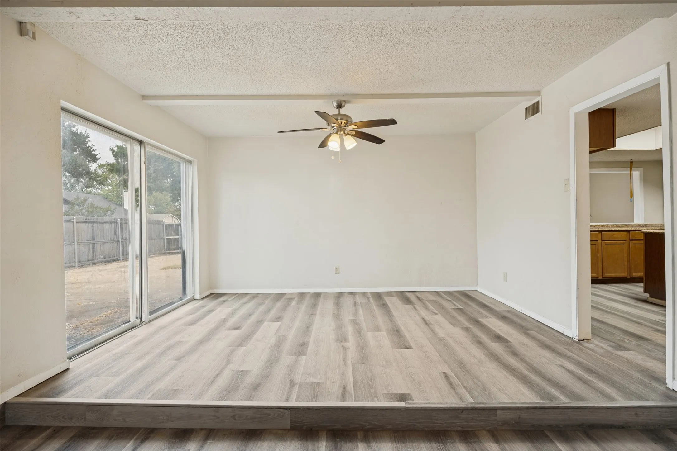 Wood-finish flooring, sliding glass door, ceiling fan with integrated lighting, and neutral wall tones