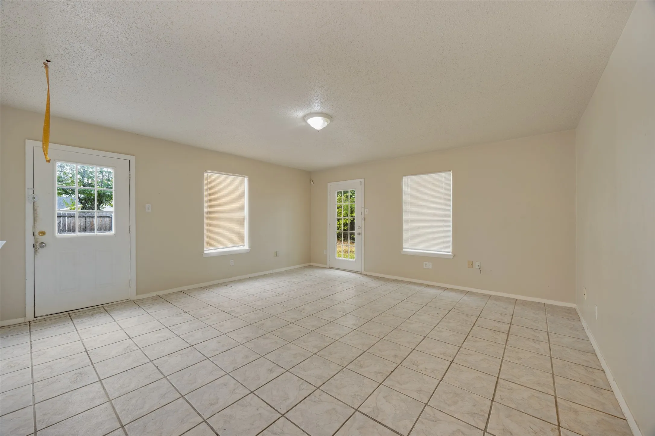 Spacious room featuring tile flooring, neutral wall paint, multiple windows, and two exterior doors