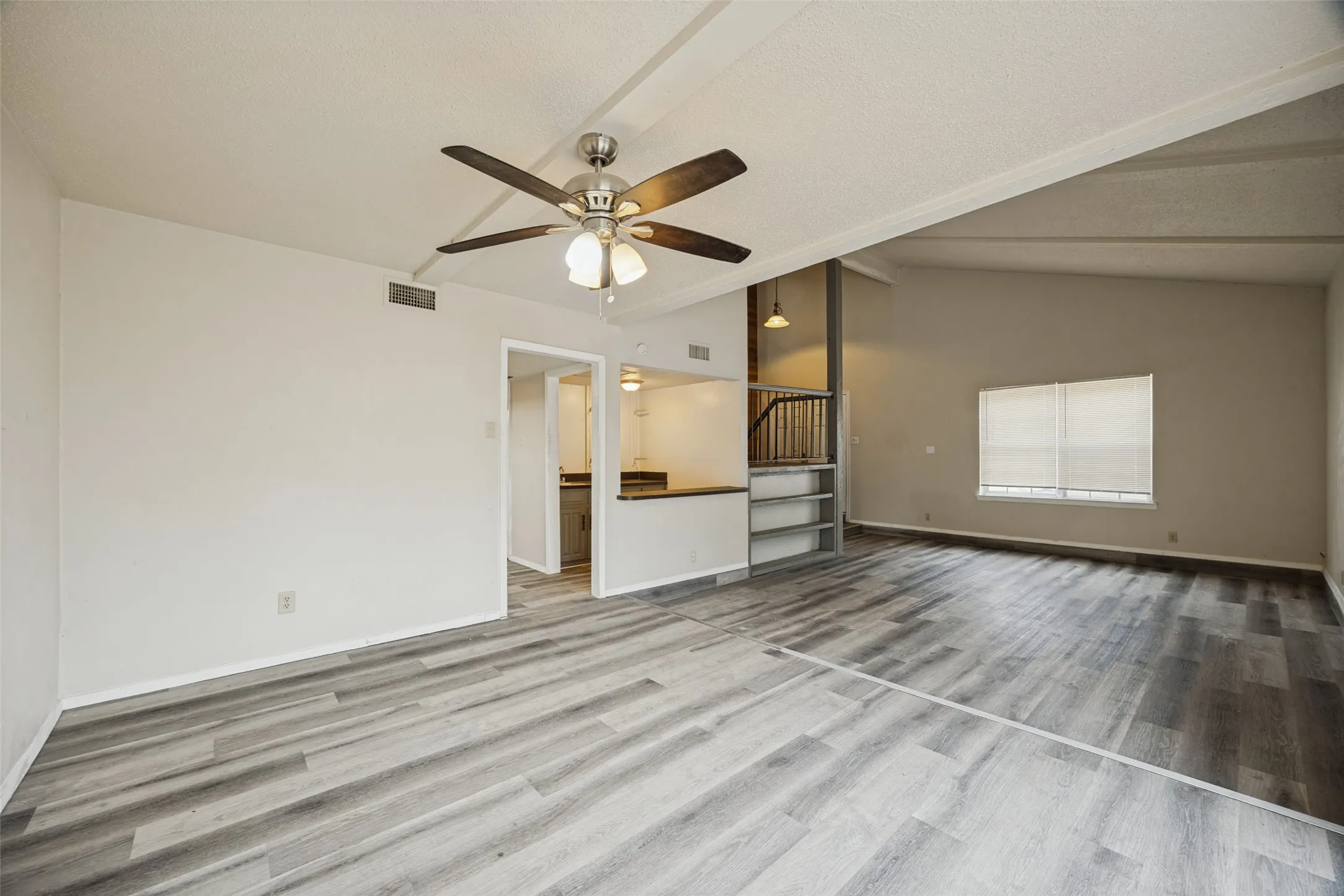 Vaulted ceiling with exposed beams, wood-finish flooring, ceiling fan with integrated lighting, built-in shelving, and a window with blinds