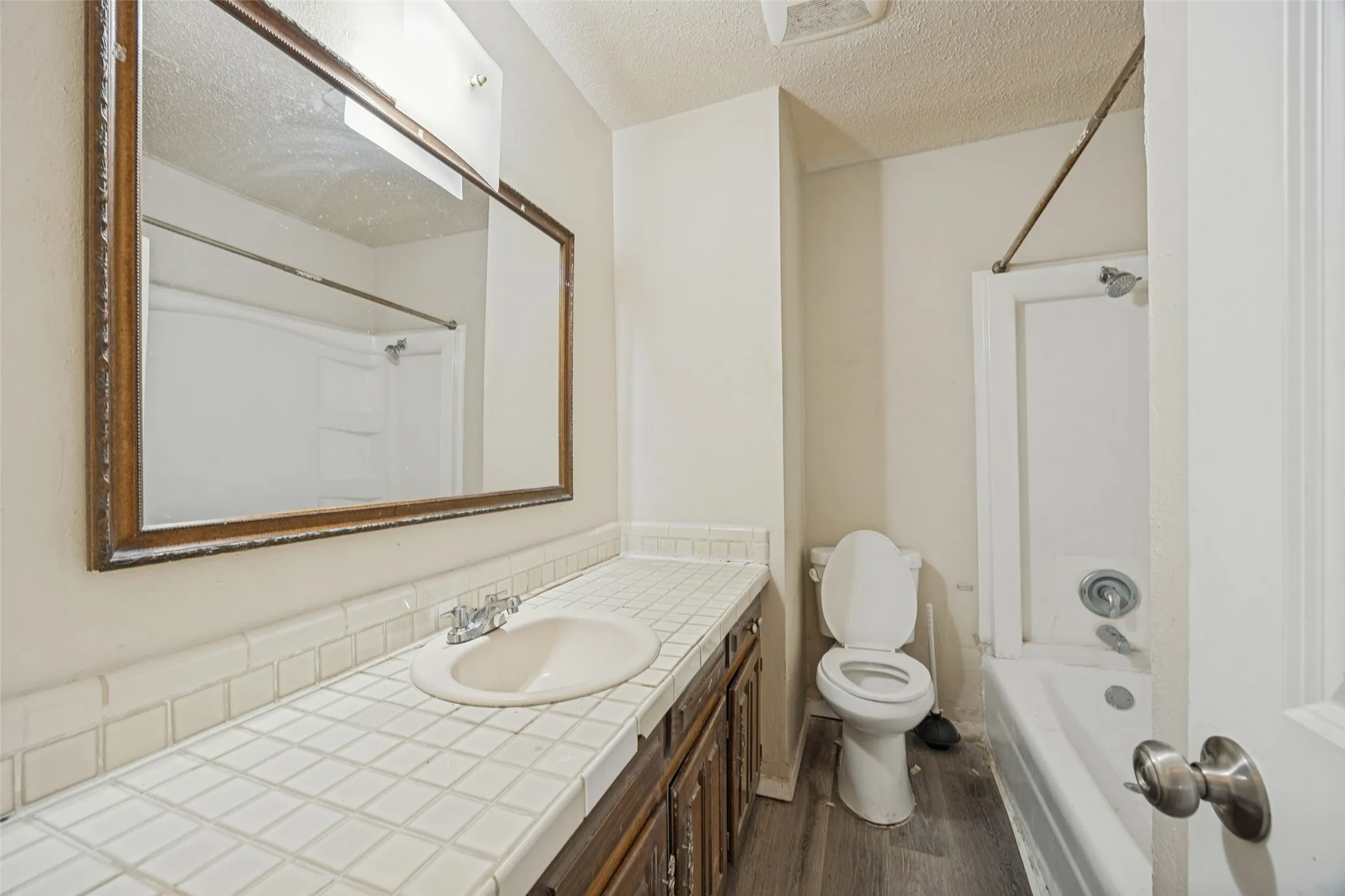 Bathroom featuring a tile countertop, integrated sink, wood-finish vanity, large wall mirror, and a shower-tub combination