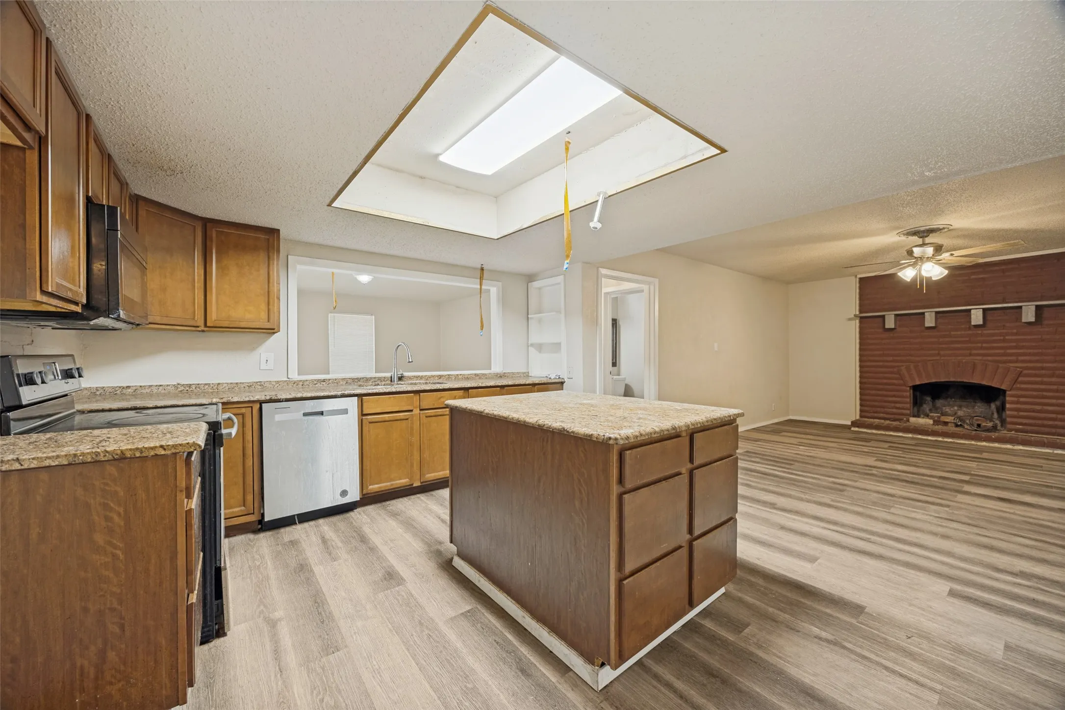 Kitchen featuring wood-finish cabinetry, granite-style countertops, stainless steel appliances, and a central island
