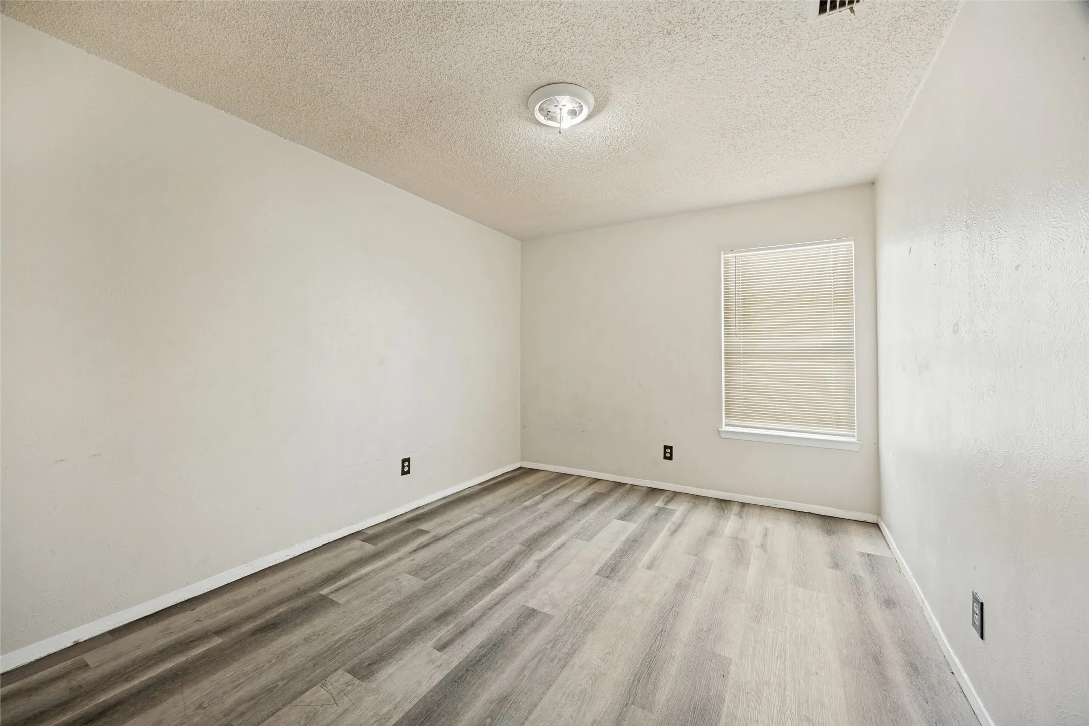 Wood-finish flooring, single window with blinds, overhead flush-mount light fixture, and textured walls