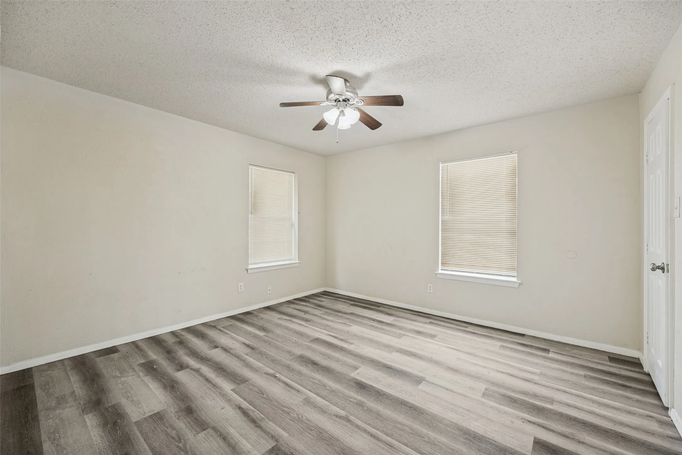 Wood-finish flooring, two windows with blinds, ceiling fan with light fixture, and white painted walls