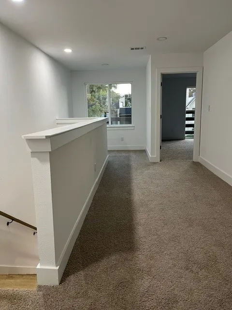 Carpeted hallway featuring a window, recessed lighting, and white trim