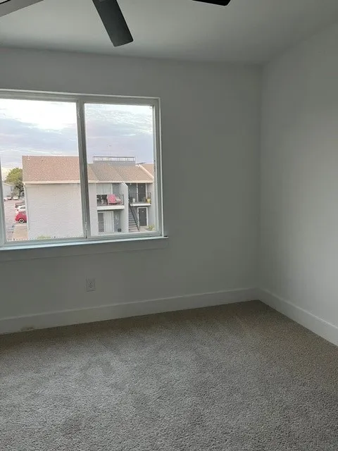 Neutral wall tones, gray carpeting, a large window, and a ceiling fan with integrated lighting