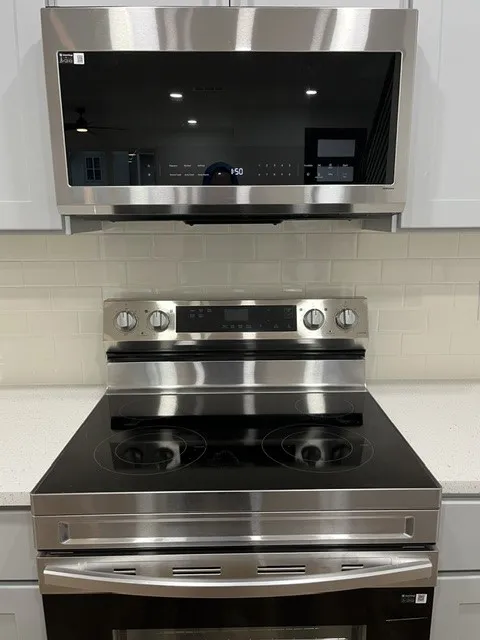Stainless steel over-the-range microwave and electric range with a black ceramic cooktop, set against a subway tile backsplash and light-toned countertops