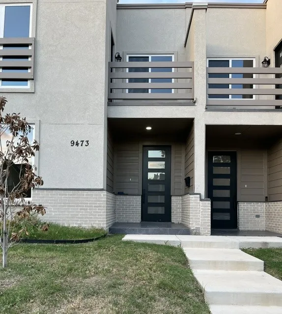 Contemporary exterior featuring multi-panel glass entry doors, a second-story balcony with slatted railing, and a brick base