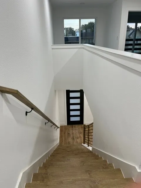 Wood-finish flooring on stairs and landing, modern full-light panel door, and multiple windows