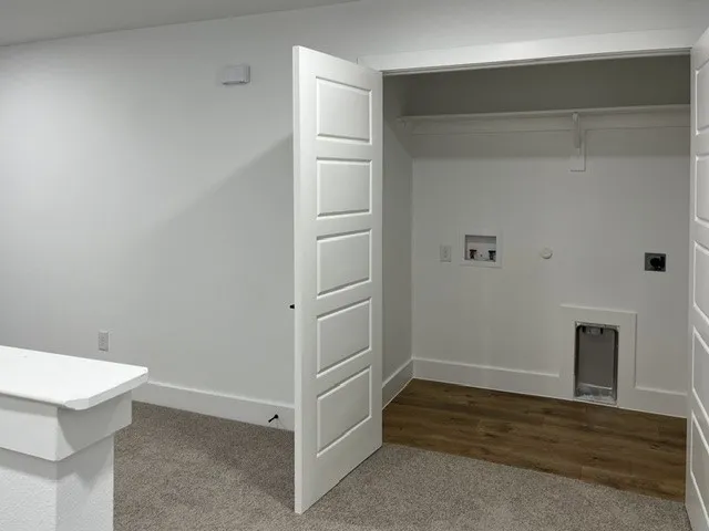 Dedicated laundry area with wood-finish flooring, white walls, and a built-in hanging rod
