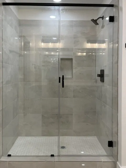 Glass-enclosed shower with matte black fixtures, a tiled shower niche, and a contrasting hexagonal tile floor