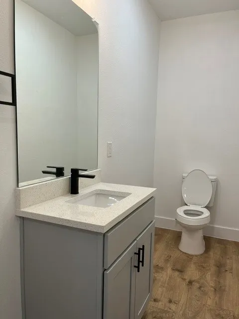 Gray vanity with matte black hardware, white countertop, integrated sink, matte black faucet, and wood-finish flooring