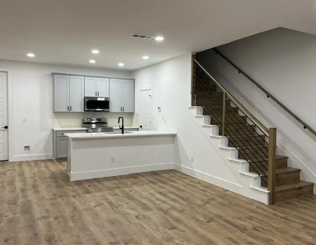 Open-concept living area with wood-finish flooring, recessed lighting, and a contemporary staircase featuring wood treads and a cable railing system