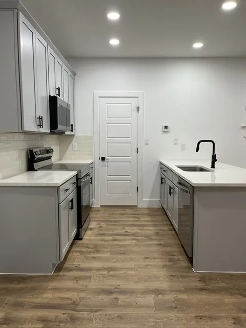 Modern kitchen featuring light gray cabinetry, white countertops, wood-finish flooring, and recessed lighting