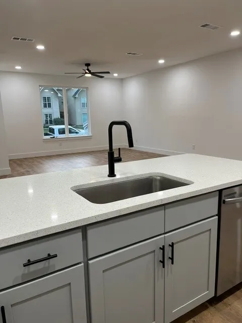 Kitchen island featuring a stainless steel undermount sink, matte black faucet, light gray cabinetry with black hardware, and an integrated dishwasher