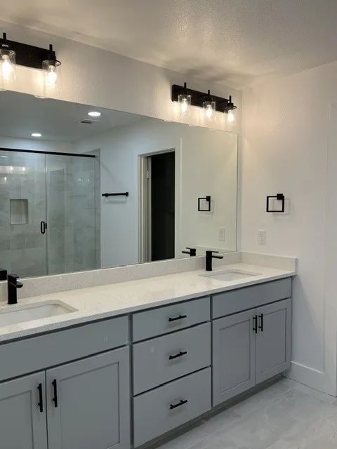 Dual vanity with light gray cabinetry, integrated sinks, white countertops, and matte black fixtures