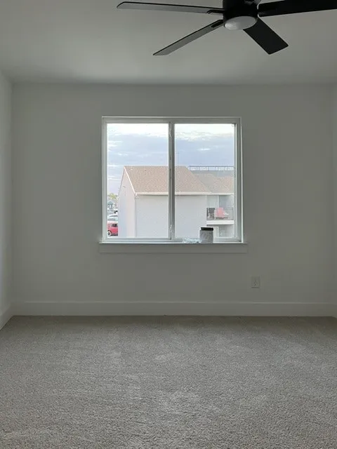 Expansive room with neutral carpeting, a large window, and a ceiling fan with integrated lighting
