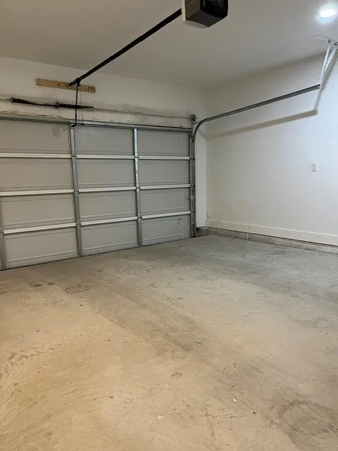 Concrete flooring with an automatic garage door opener system, white walls, and recessed lighting
