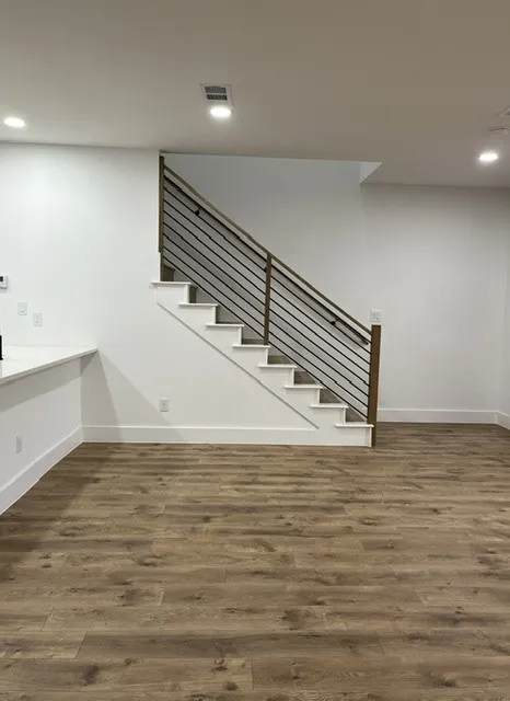 Wood-finish flooring, staircase with metal and wood railing, recessed ceiling lighting, and white baseboards