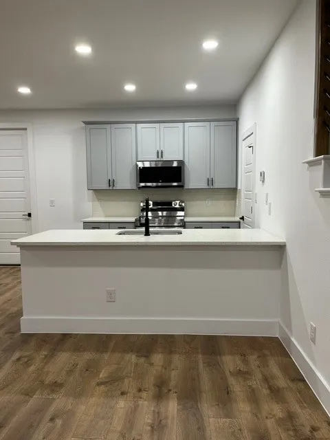 Kitchen featuring a stone-finish countertop, wood-finish flooring, recessed lighting, stainless steel appliances, and gray cabinetry