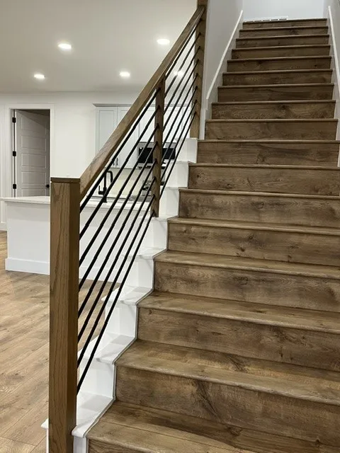 Staircase with wood-finish treads and risers, black metal balusters, and a natural wood handrail