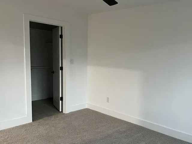 Neutral color palette, plush carpet flooring, white trim, solid core door, and a built-in closet with shelving and hanging rod