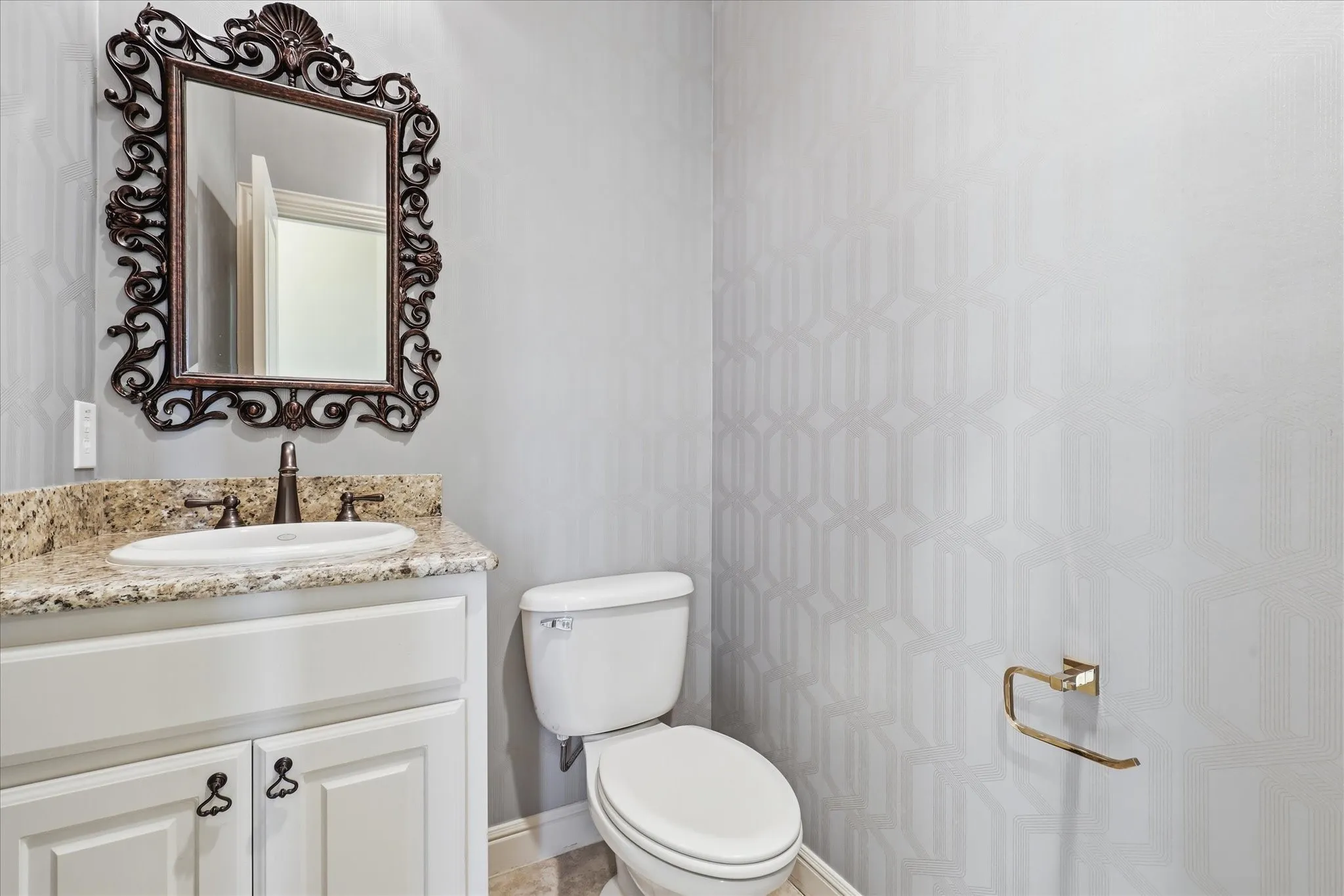 Powder room featuring a white vanity cabinet with stone countertop, drop-in sink, ornate wall mirror, and textured wallpaper