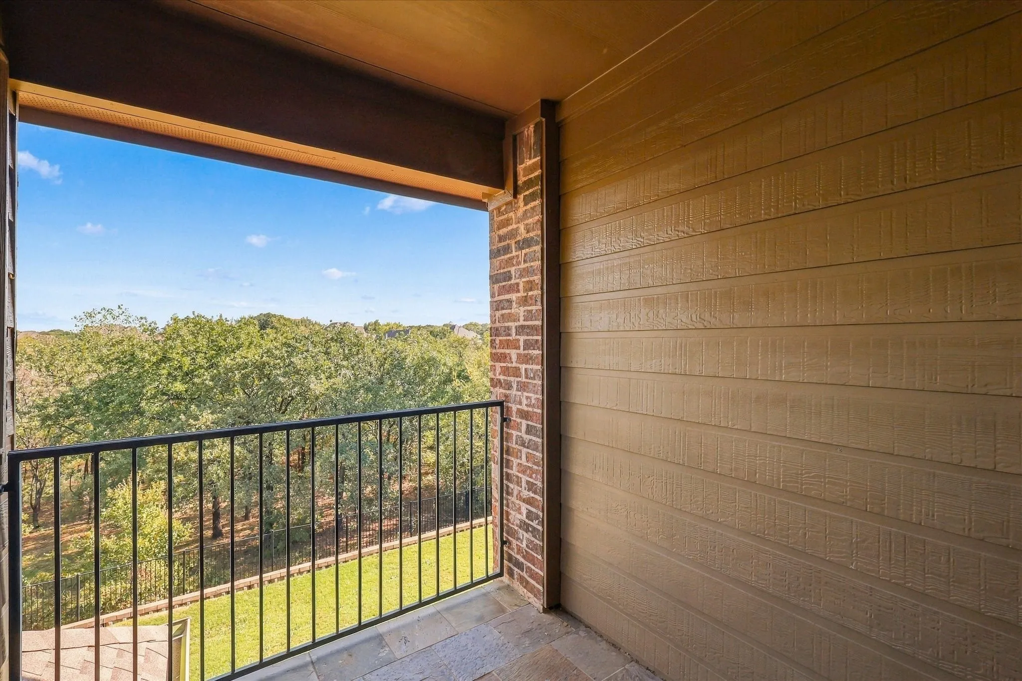 Covered balcony featuring horizontal lap siding, brick masonry detailing, tile flooring, and a metal railing
