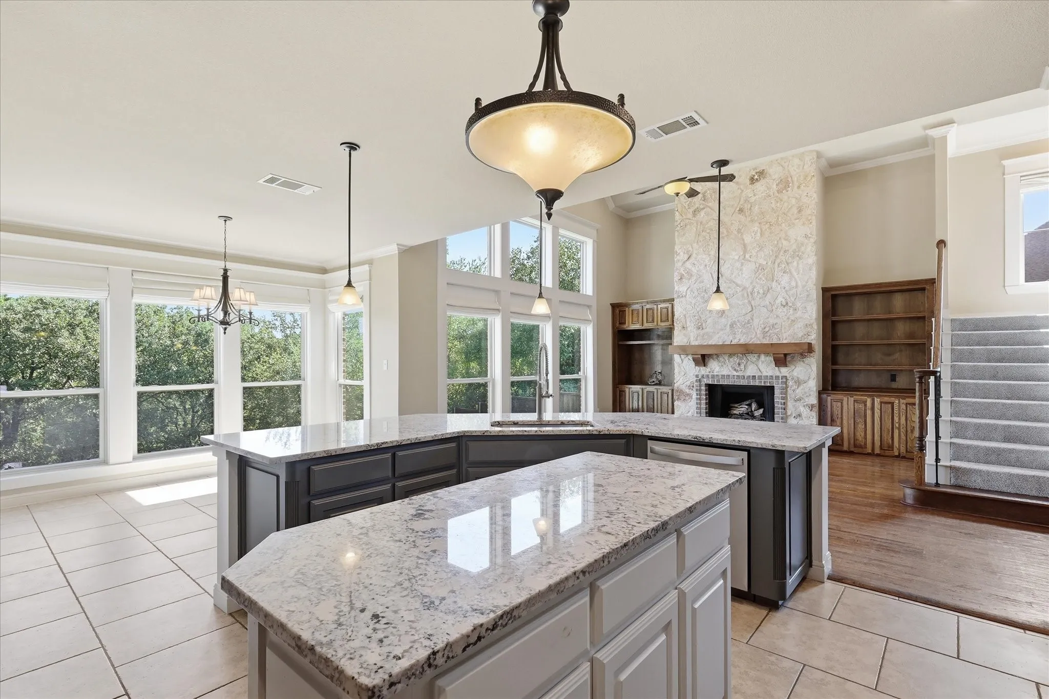 Kitchen island featuring stone countertops and dual-tone cabinetry, floor-to-ceiling stone fireplace, built-in wooden shelving, and expansive windows