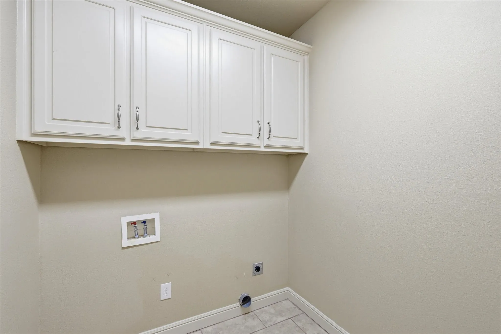 Utility space featuring wall-mounted white cabinetry with shaker-style doors, tile flooring, and dedicated plumbing connections