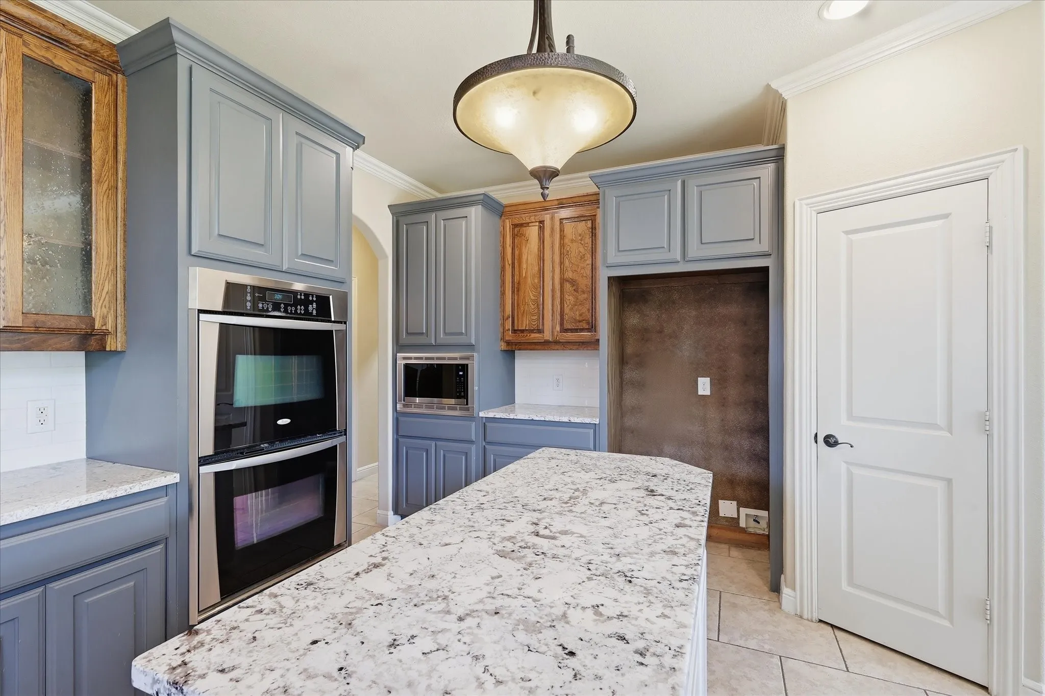 Kitchen featuring slate-blue and natural wood-tone cabinetry, speckled stone countertops, a stainless steel double wall oven, and a pendant light fixture