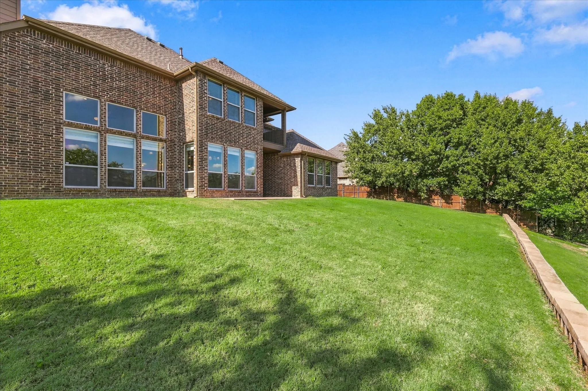 Multi-level brick exterior featuring expansive windows and a large manicured lawn with a stone retaining wall