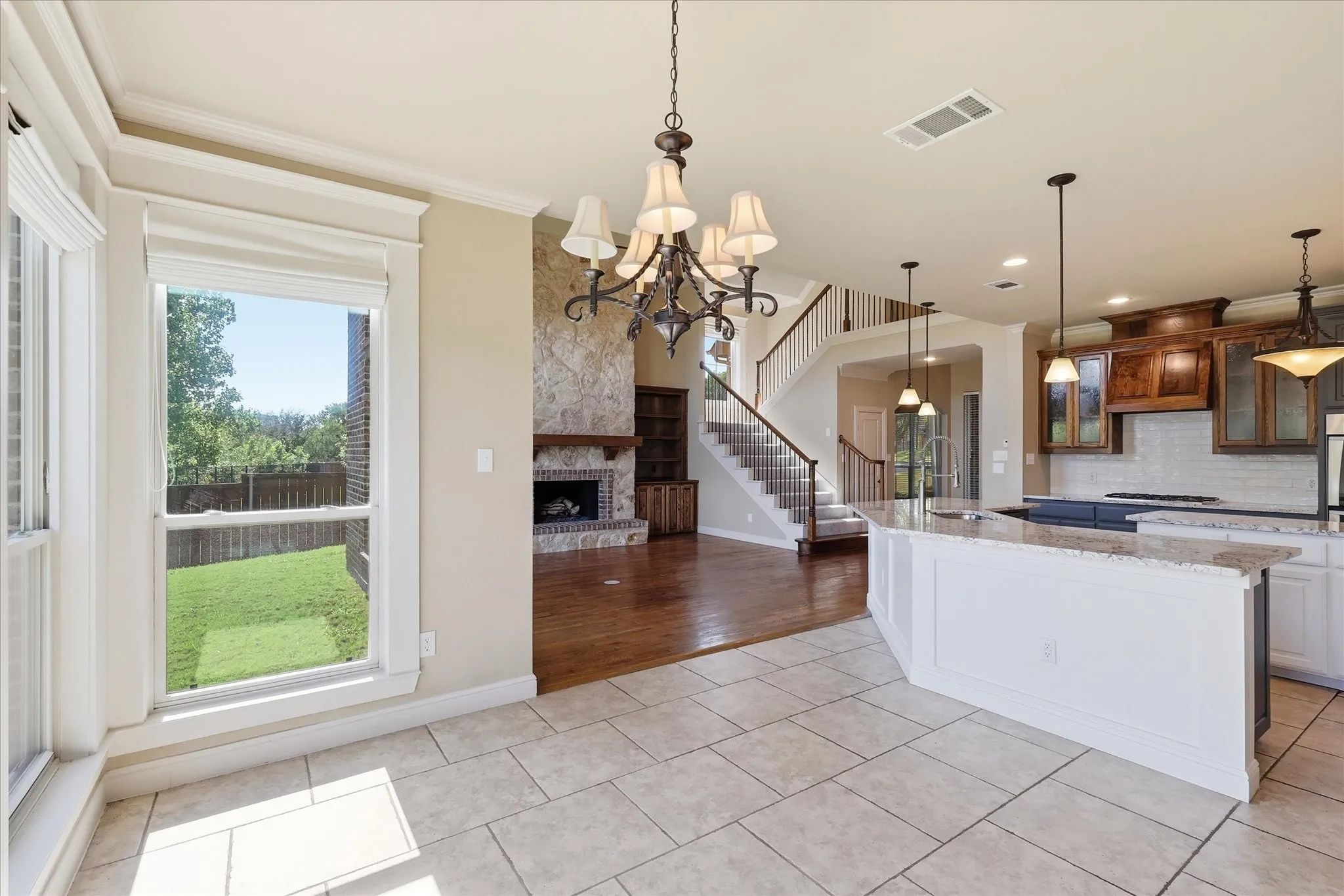 Open-concept space featuring stone-facade fireplace, wood-finish flooring, tile flooring, tiered center island with countertop, and classic chandelier lighting