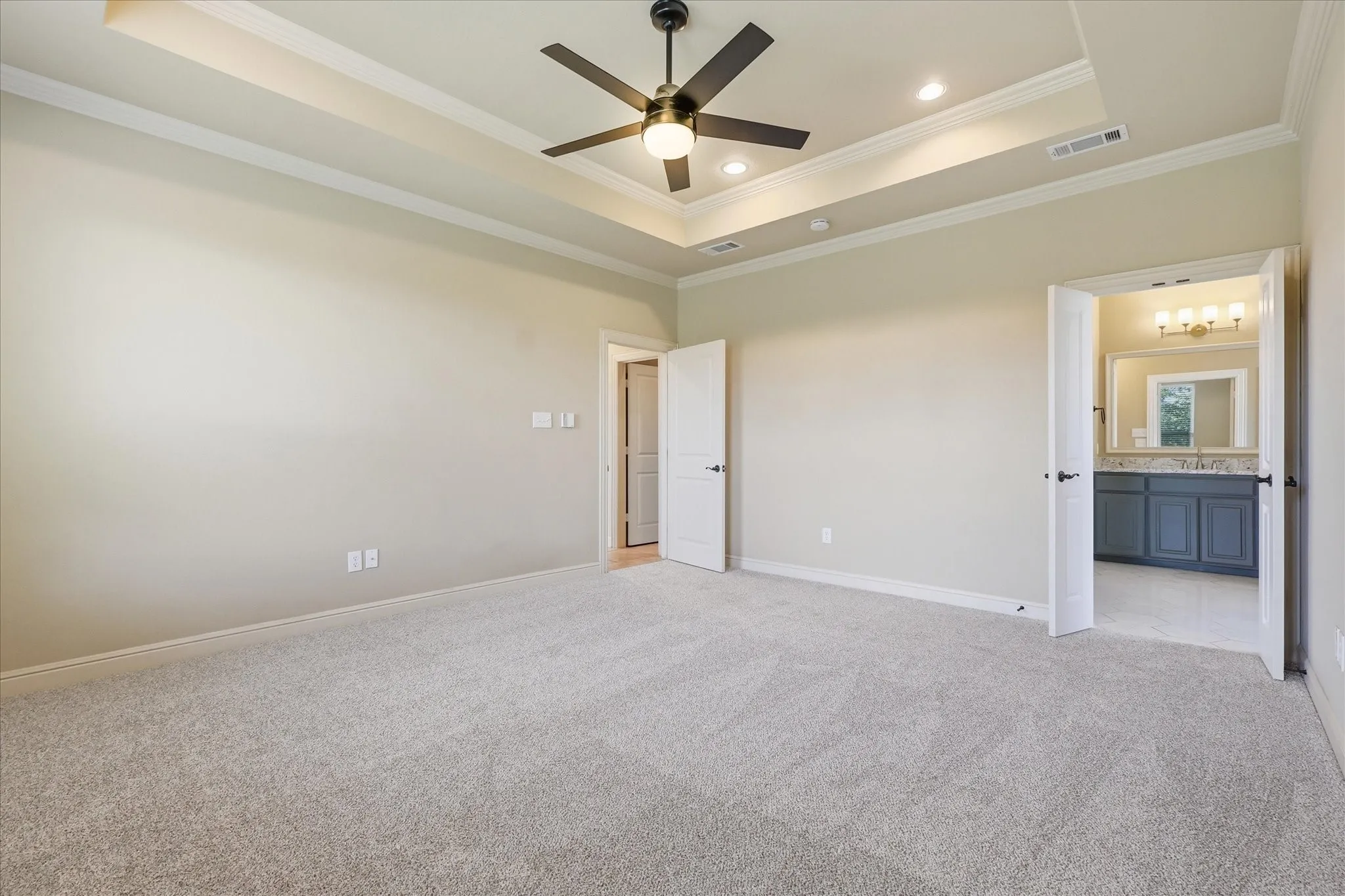 Tray ceiling with recessed lighting, ceiling fan with integrated lighting, neutral wall-to-wall carpeting, and double-door entry