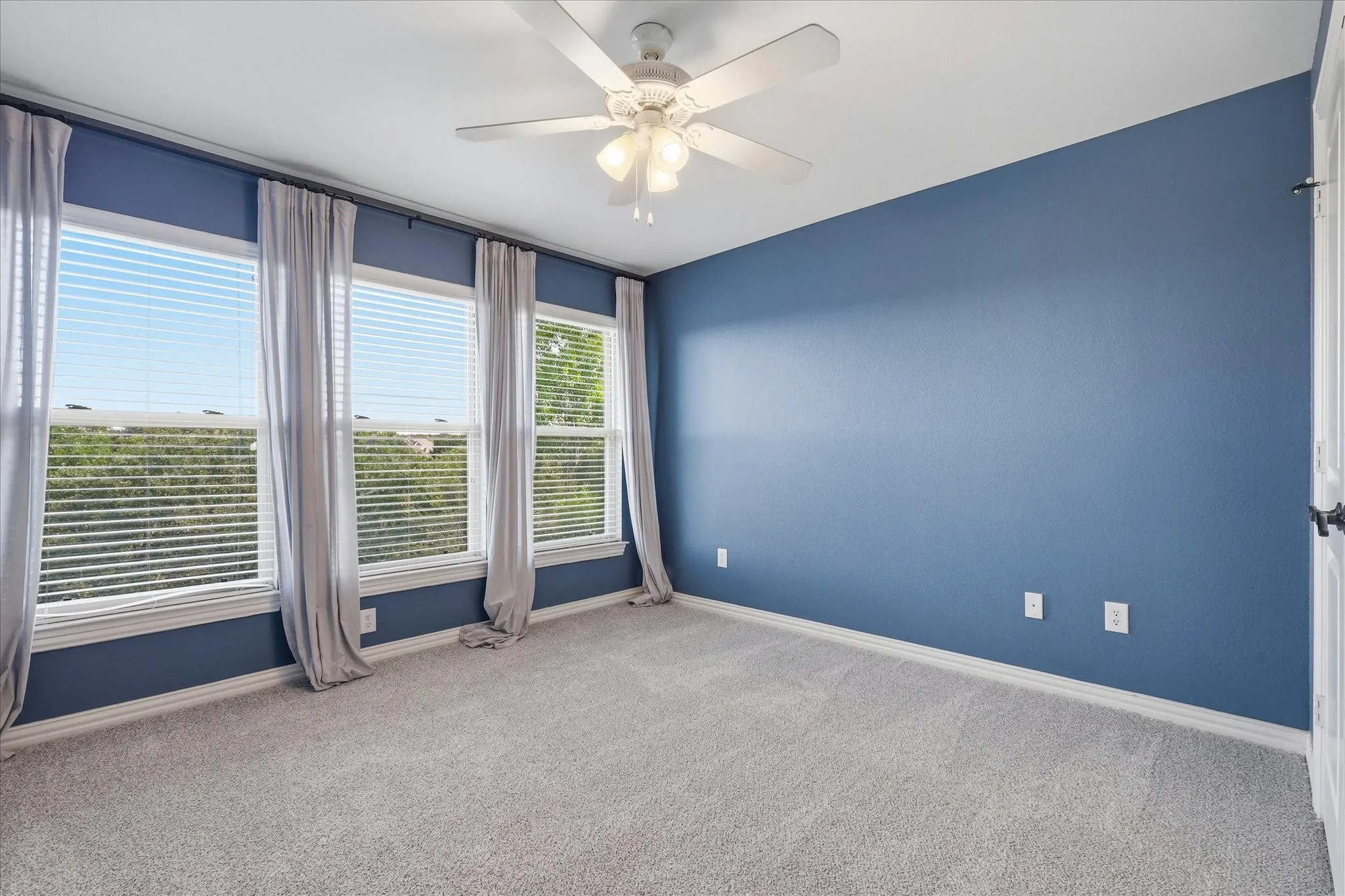 Neutral-toned wall-to-wall carpeting, three multi-pane windows, and a central ceiling fan with integrated lighting