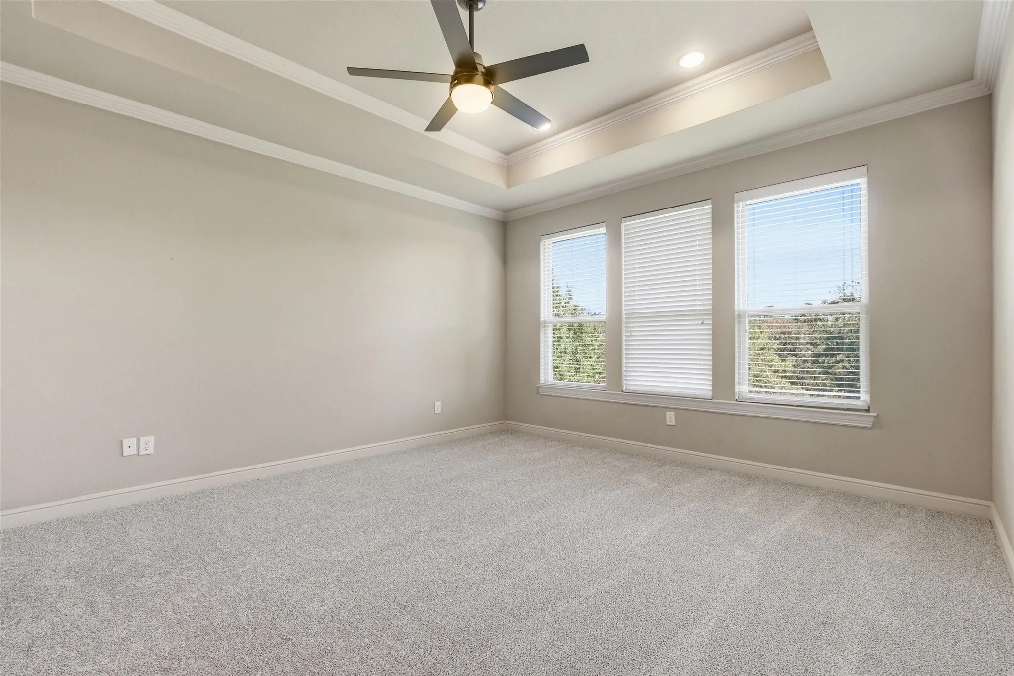 Tray ceiling featuring crown molding, neutral carpeting, recessed lighting, and a modern ceiling fan with integrated lighting