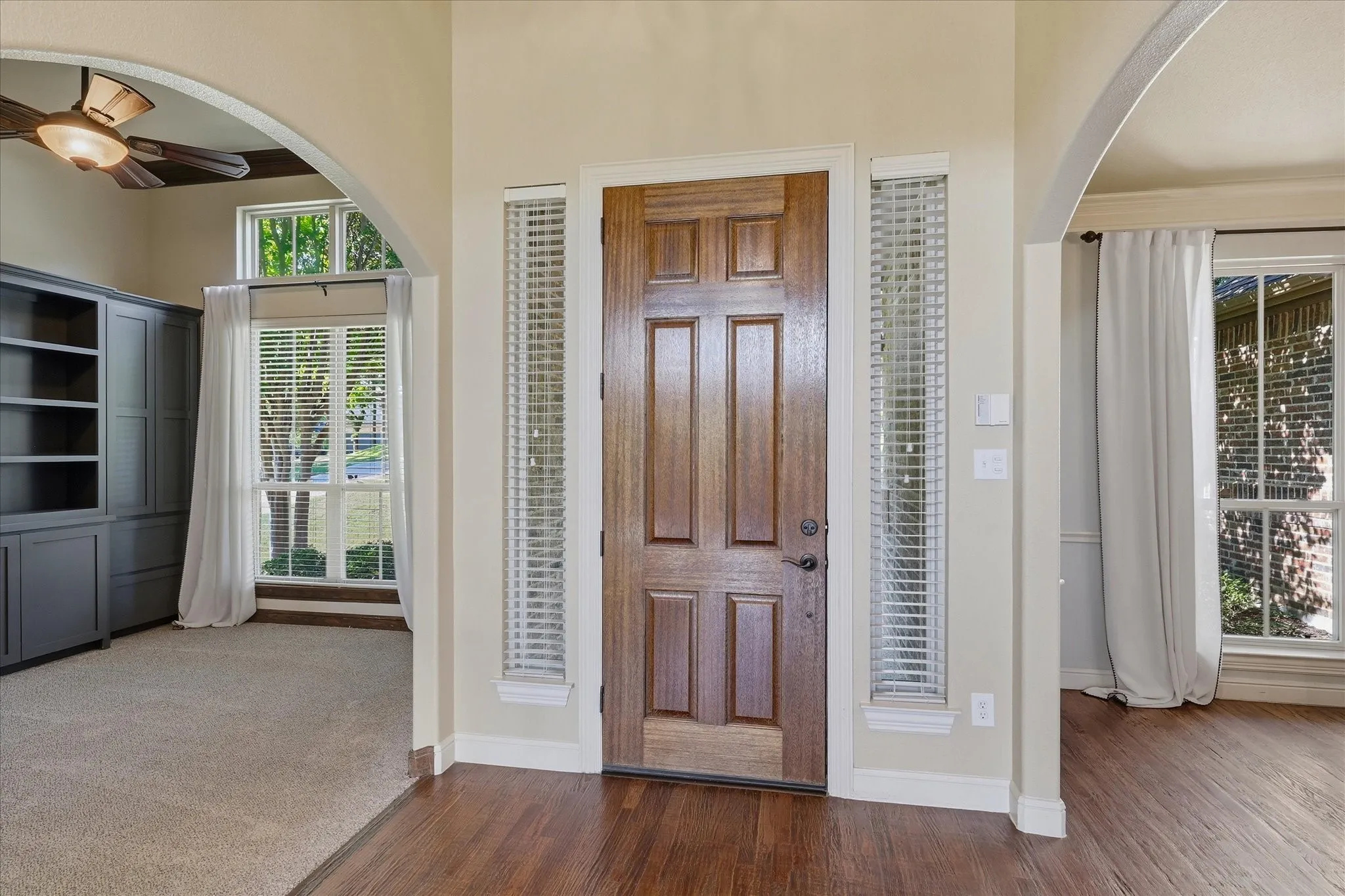 Entryway featuring a solid wood front door with sidelights, arched architectural detailing, built-in cabinetry, and wood-finish flooring