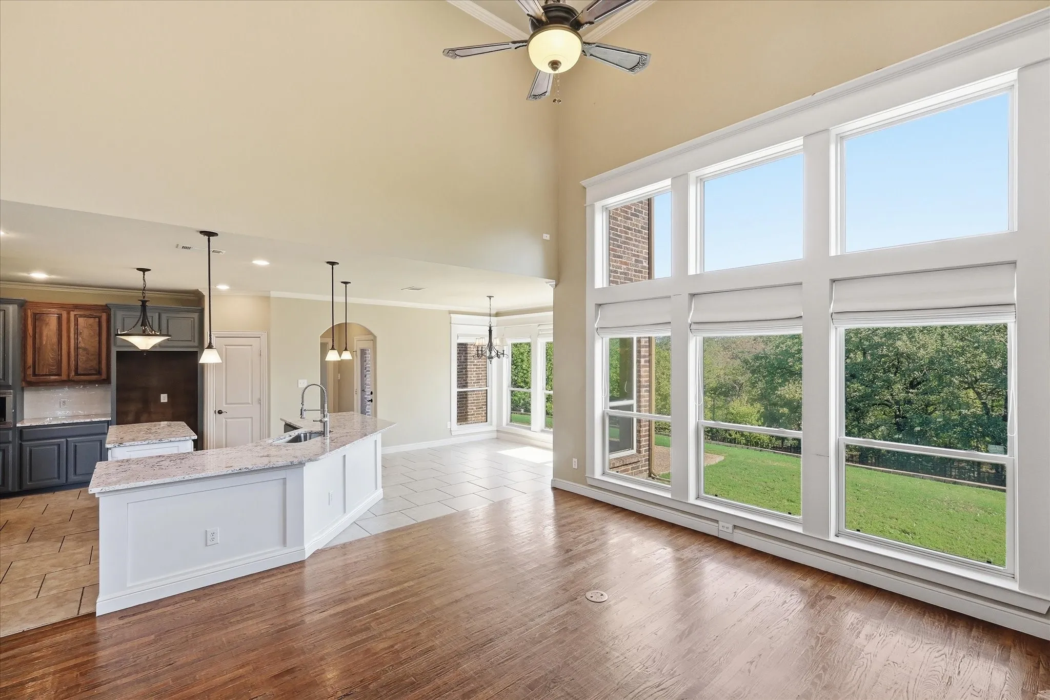 Vaulted ceiling with integrated paddle fan, expansive multi-pane windows, wood-finish flooring, and kitchen featuring a stone-surface island and built-in cabinetry