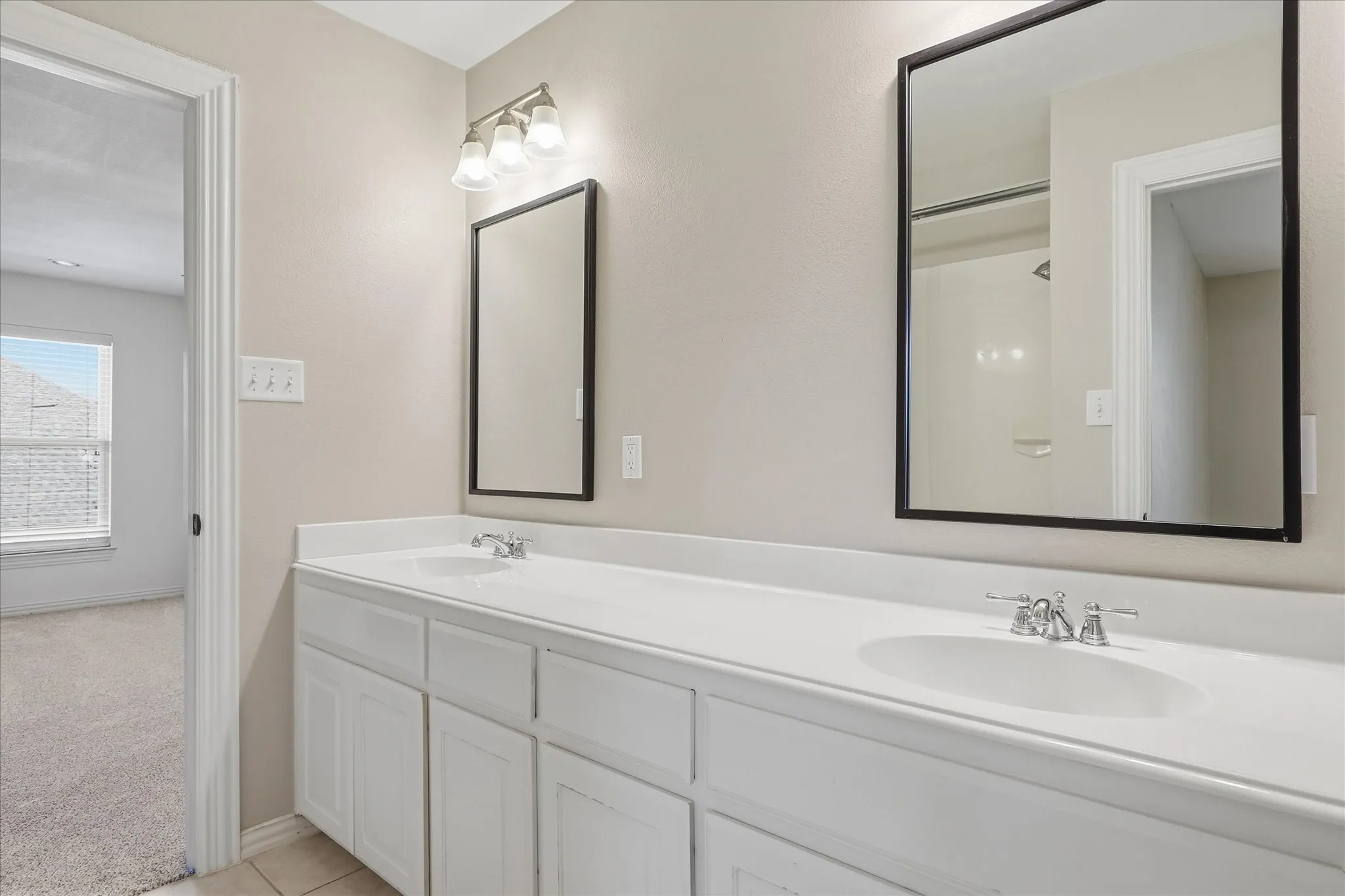 Double vanity featuring white cabinetry, integrated dual-basin countertop, black-framed mirrors, and polished chrome faucets
