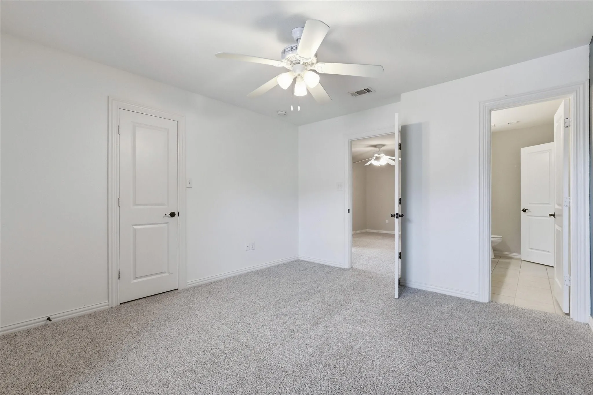 Neutral-toned carpeted flooring, white interior doors, and a ceiling-mounted light fixture with a multi-blade fan