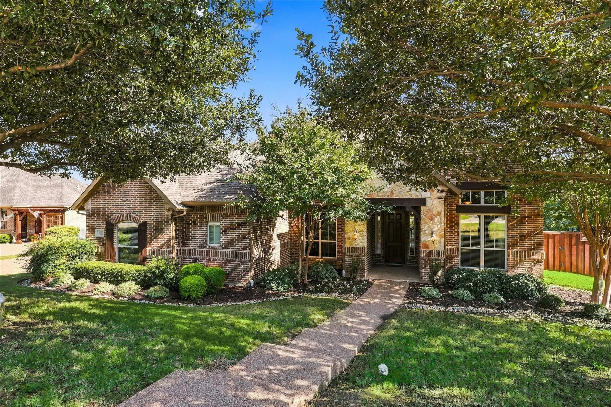 Traditional brick exterior featuring stone accents, arched windows with shutters, a multi-gabled roofline, and a paved walkway