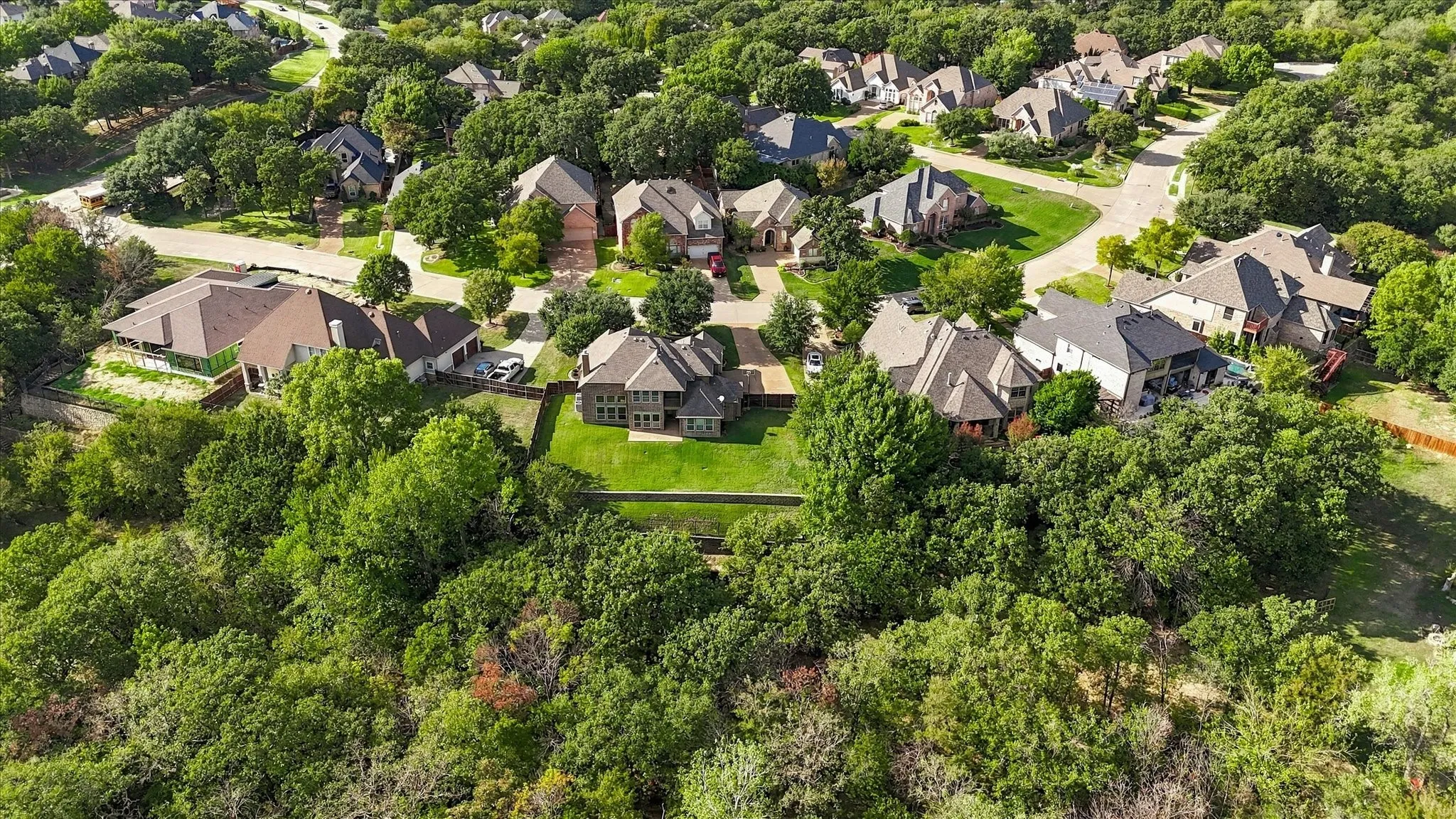 Aerial perspective of a multi-story residence featuring a steep-pitched roofline, stone exterior facade, and a grass-covered backyard bordering a dense treeline