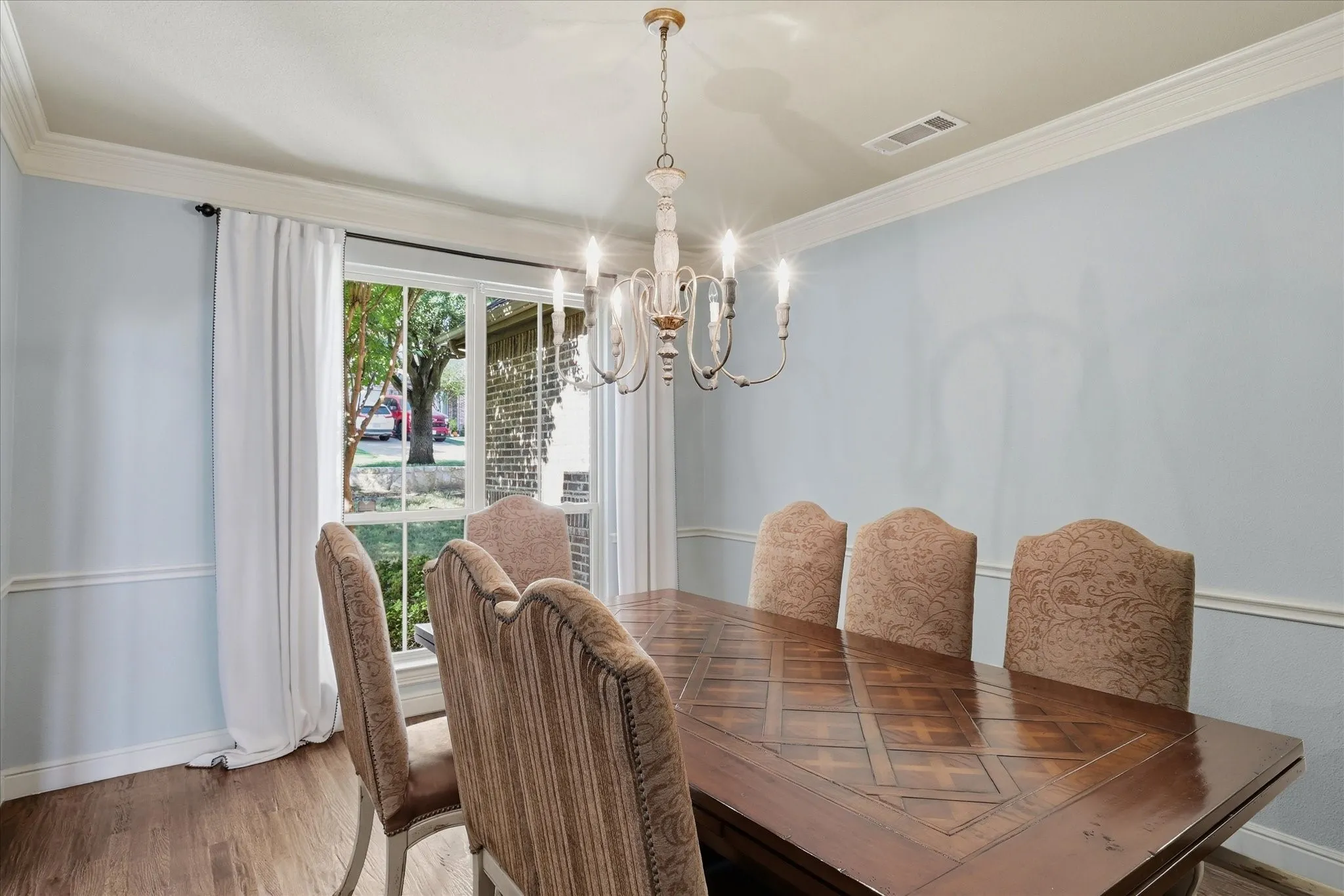 Multi-pane window, crown molding, chair rail trim, and a multi-arm candelabra-style chandelier featuring wood-finish flooring