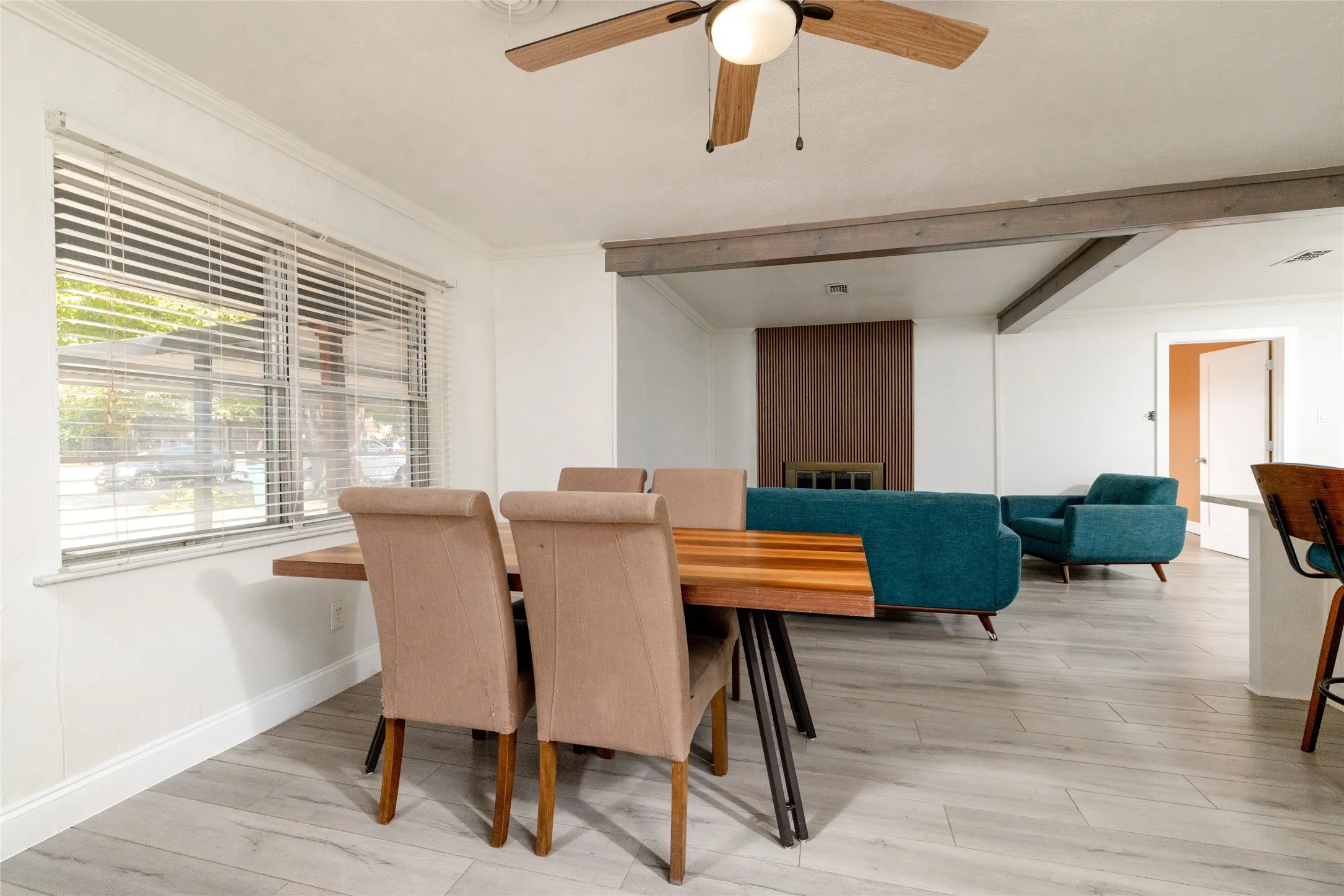 Wood-finish flooring throughout, ceiling fan with integrated lighting, exposed beam accents, and a fireplace with a wood-paneled surround